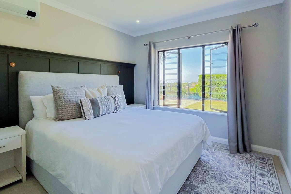 A well-maintained bedroom featuring wainscoting, recessed lighting, a wall-mounted air conditioning unit, and large casement windows providing natural light.