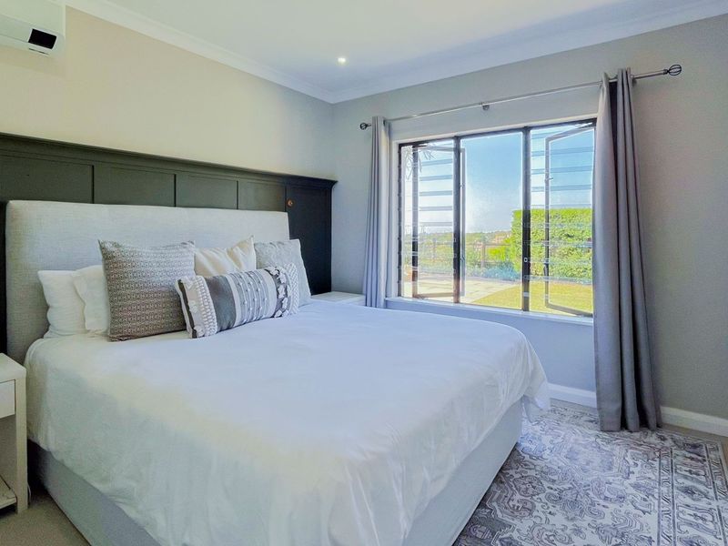 A well-maintained bedroom featuring wainscoting, recessed lighting, a wall-mounted air conditioning unit, and large casement windows providing natural light.