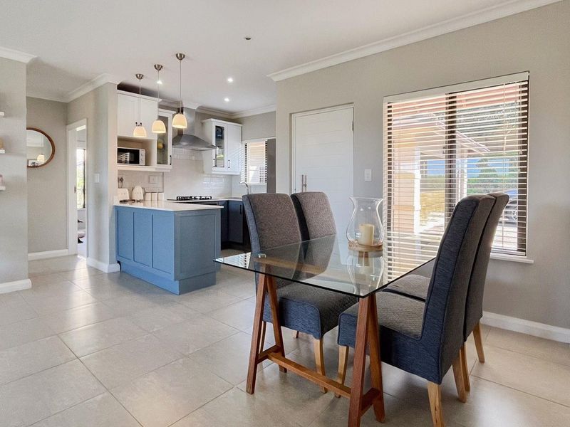 Modern open-plan kitchen and dining area featuring a central island, sleek cabinetry, tiled flooring, and ample natural light through large windows.