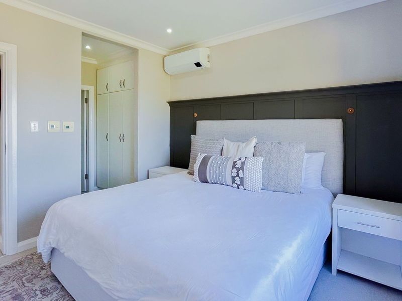 A well-maintained bedroom featuring a dark panelled headboard wall, built-in storage cupboards, and a wall-mounted air conditioning unit.