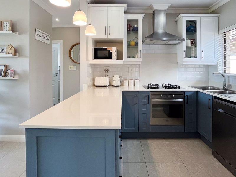 Modern kitchen featuring two-tone cabinetry, stone countertops, subway tile backsplash, and integrated stainless steel appliances with a functional breakfast bar island.