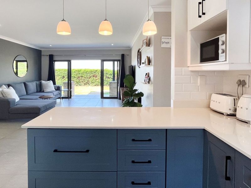 Modern open-plan living area featuring a contemporary kitchen with blue cabinetry, quartz countertops, and seamless flow to the outdoor patio through sliding glass doors.