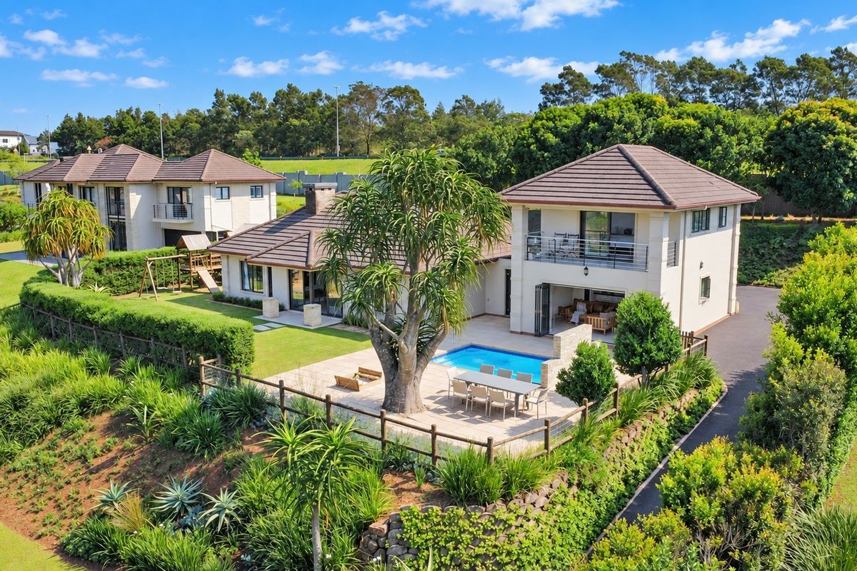 Aerial view of a well-maintained residential property featuring a swimming pool, spacious patio, landscaped garden, and a balcony overlooking the grounds.
