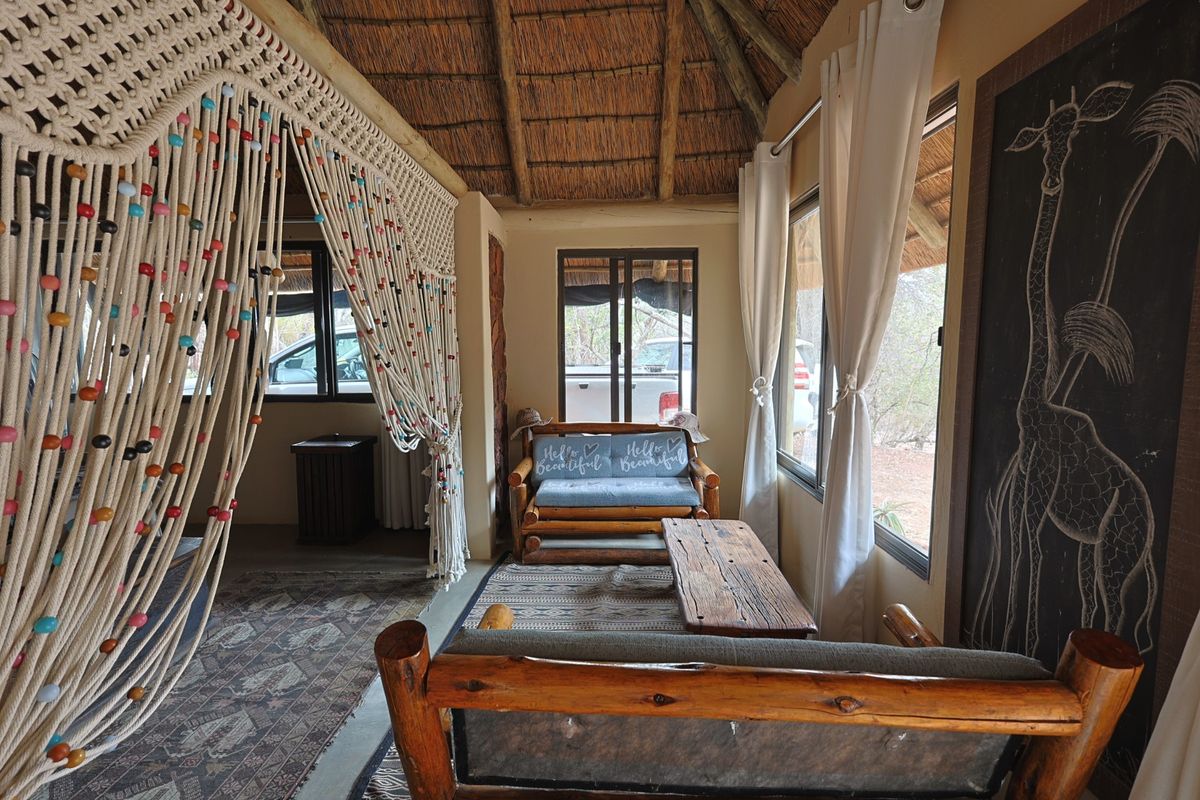 A rustic living area featuring a traditional thatched roof with exposed timber rafters and large windows providing natural light.