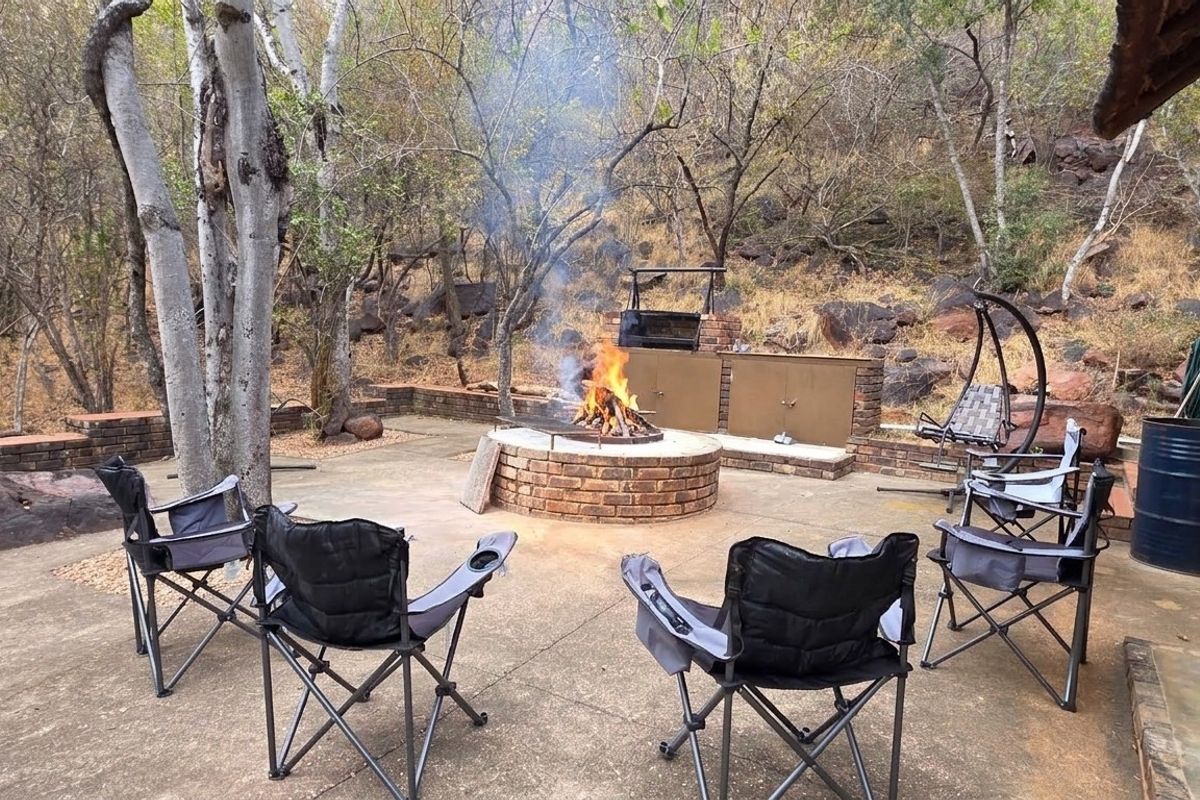 Outdoor entertainment area featuring a brick fire pit and built-in braai, set against a natural bushveld backdrop.