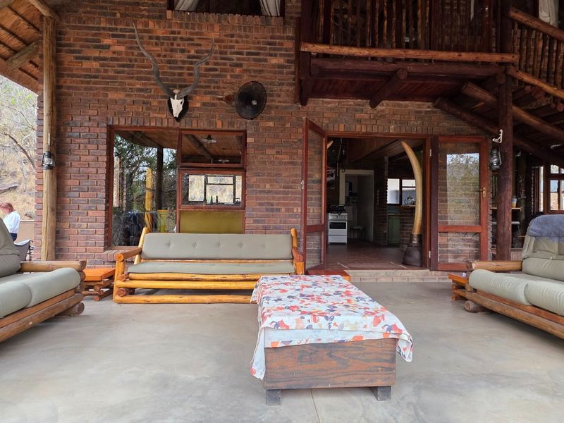 A spacious covered patio featuring exposed brickwork, timber structural elements, and a staircase leading to an upper level, offering a rustic outdoor living space.