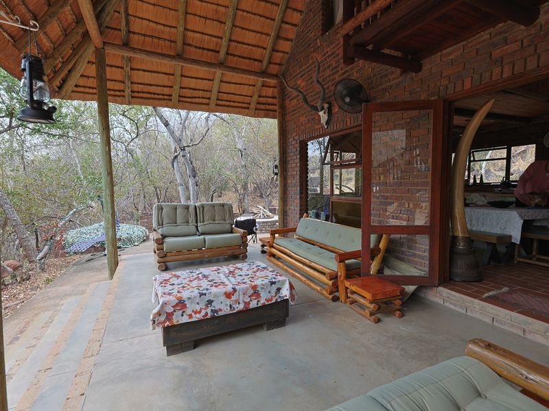 A spacious covered patio featuring a rustic thatched roof, exposed brickwork, and concrete flooring, offering a seamless transition to the natural outdoor surroundings.