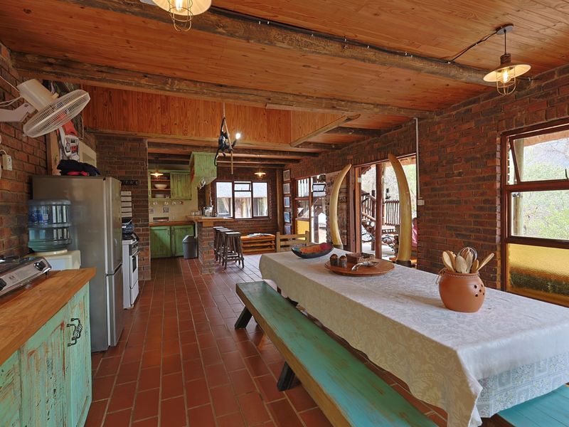 Open-plan kitchen and dining area featuring rustic exposed brick walls, timber ceilings, terracotta flooring, and direct access to an outdoor patio.