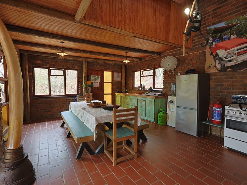 Open-plan living and kitchen area featuring rustic exposed brick walls, timber beam ceilings, tiled flooring, and functional kitchen cabinetry with a freestanding oven.