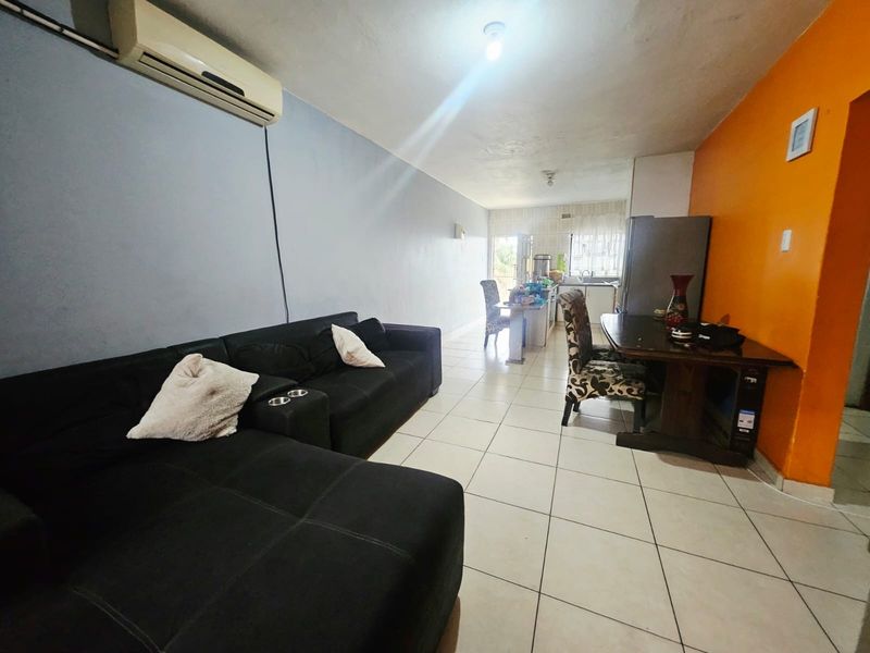 Open-plan living and kitchen area featuring tiled flooring and a wall-mounted air conditioning unit, providing a functional combined living and dining space.