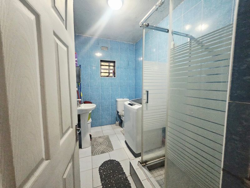 A functional bathroom featuring blue wall tiles, a pedestal basin, a toilet, and a glass-enclosed shower area.