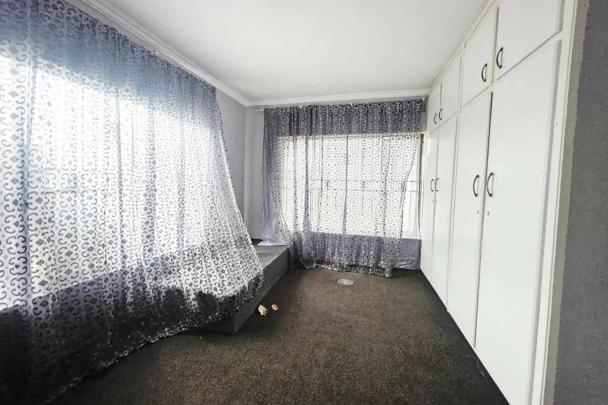 A vacant bedroom featuring built-in cupboards, carpeted flooring, and large windows with curtain rails, offering a blank canvas for renovation.