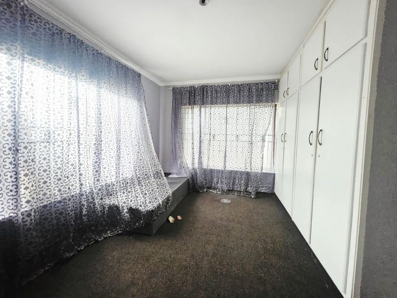 A vacant bedroom featuring built-in cupboards, carpeted flooring, and large windows with curtain rails, offering a blank canvas for renovation.