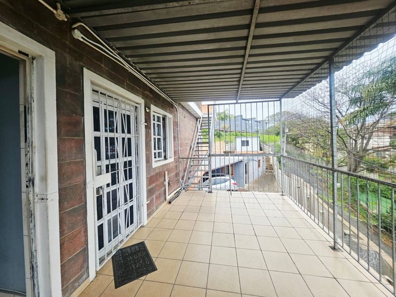 A covered outdoor balcony featuring tiled flooring, metal security fixtures, and an external staircase, providing access to the property's exterior areas.