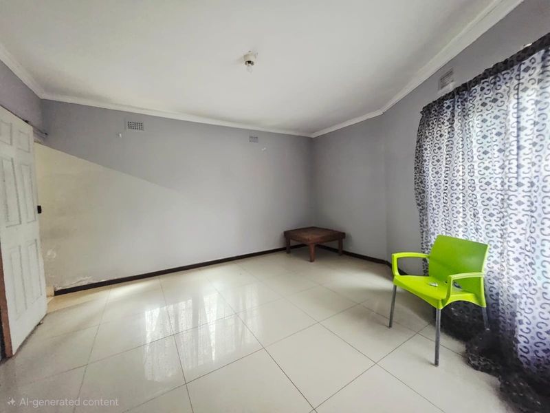A sparsely furnished living area featuring light-colored floor tiles, neutral wall paint, and decorative window curtains.