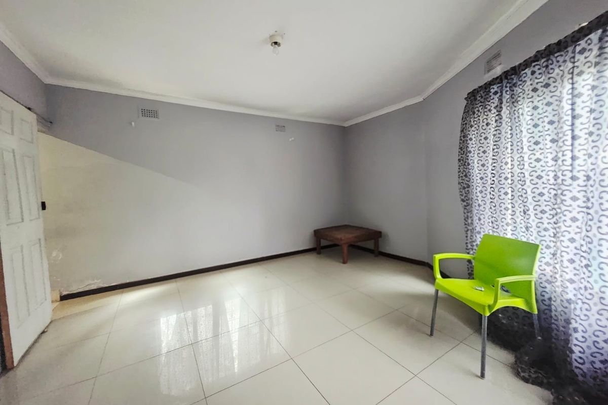 A sparsely furnished living area featuring light-colored floor tiles, neutral wall paint, and decorative window curtains.