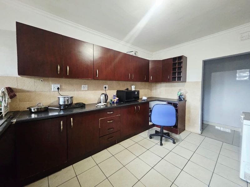 A functional kitchen featuring dark wood cabinetry, tiled backsplash, and ceramic flooring, offering a practical layout with ample storage space.