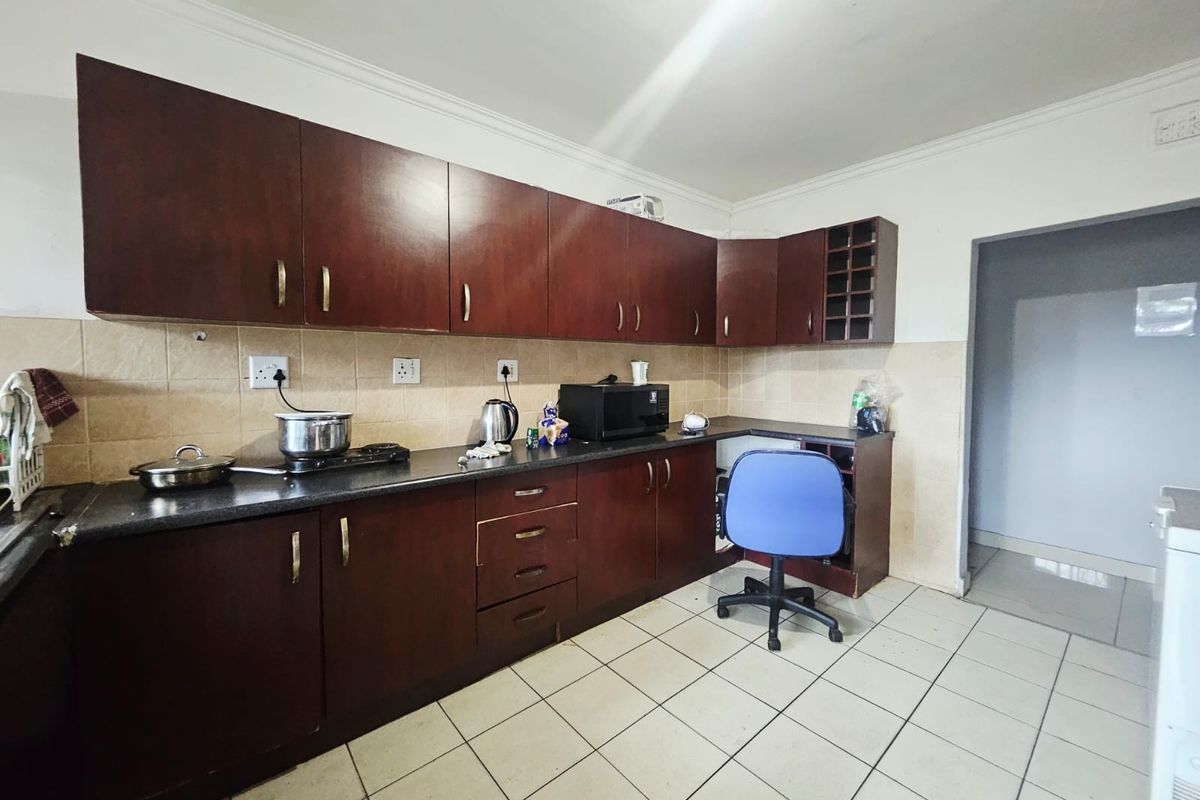 A functional kitchen featuring dark wood cabinetry, tiled backsplash, and ceramic flooring, offering a practical layout with ample storage space.