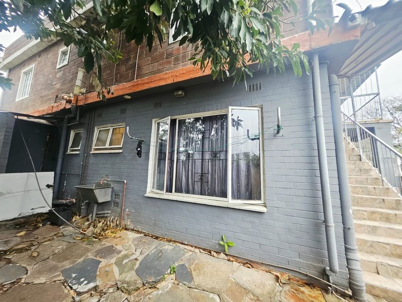 Rear exterior view of the property featuring painted brick walls, stone paving, an external utility sink, and an outdoor staircase.