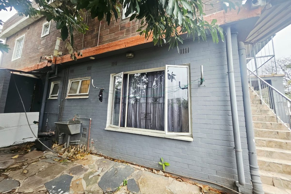 Rear exterior view of the property featuring painted brick walls, stone paving, an external utility sink, and an outdoor staircase.