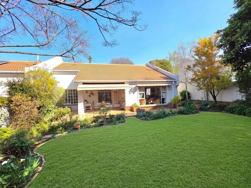 A well-maintained rear townhouse elevation featuring a paved patio with a retractable awning, overlooking a lush, landscaped garden with a manicured lawn.