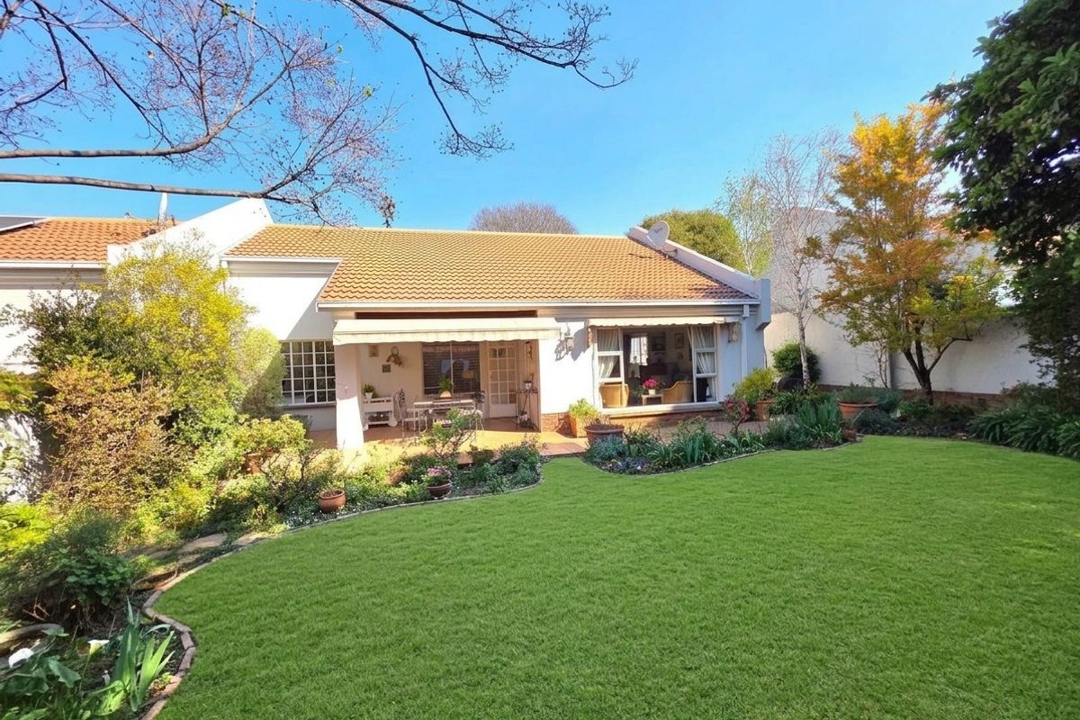 A well-maintained rear townhouse elevation featuring a paved patio with a retractable awning, overlooking a lush, landscaped garden with a manicured lawn.