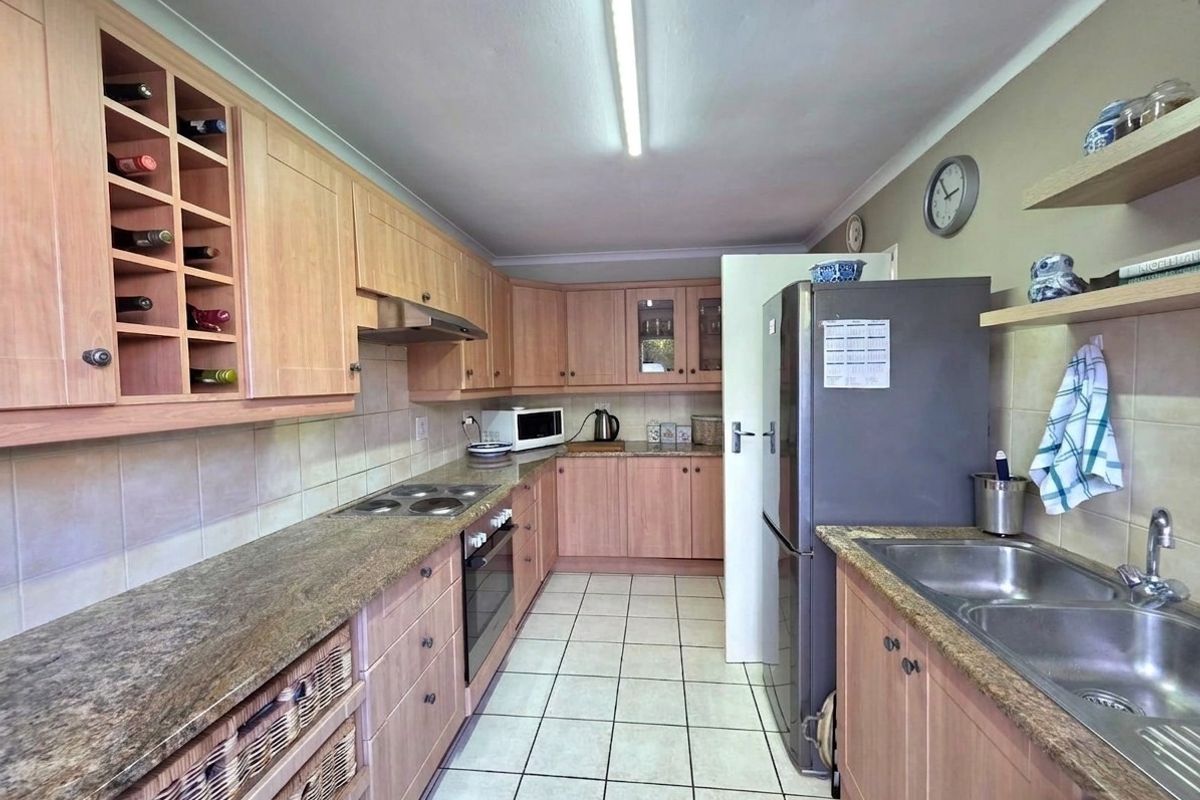 Functional galley-style kitchen featuring light wood cabinetry, laminate countertops, integrated oven and hob, and tiled flooring with ample storage space.