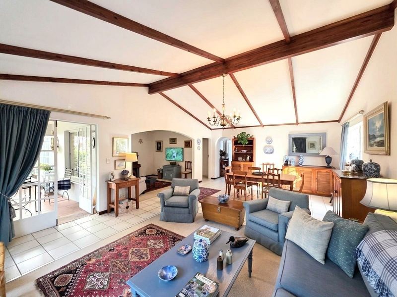 Spacious open-plan living and dining area featuring vaulted ceilings with exposed timber beams, tiled flooring, and direct access to an outdoor patio.