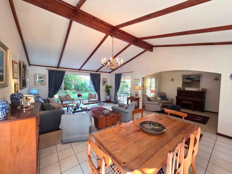 Spacious open-plan living and dining area featuring exposed timber ceiling beams, tiled flooring, and large windows providing natural light and garden views.