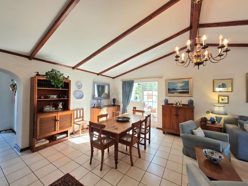 Spacious open-plan living and dining area featuring vaulted ceilings with exposed timber beams, tiled flooring, and direct access to the patio through french doors.