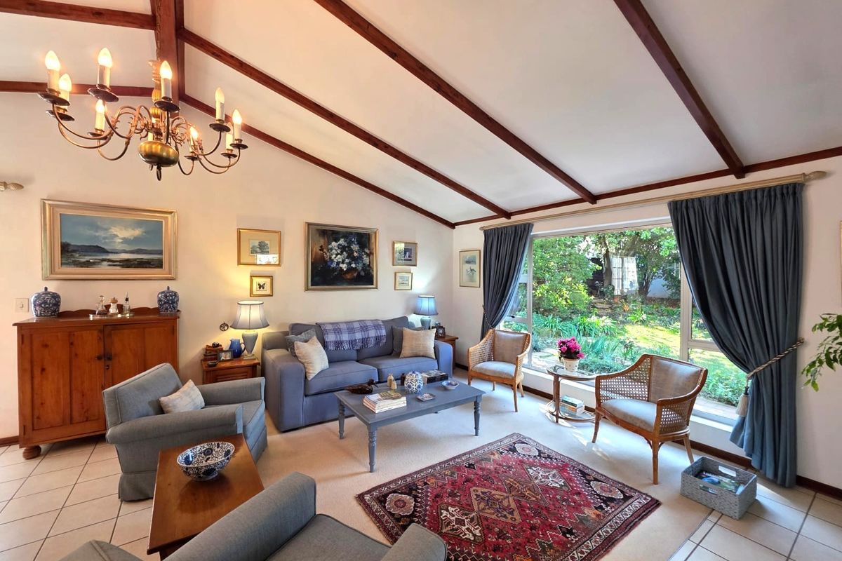 Spacious living room featuring a vaulted ceiling with exposed timber beams, large picture window overlooking the garden, and tiled flooring.
