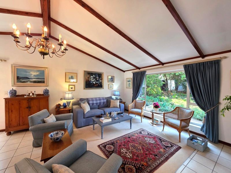 Spacious living room featuring a vaulted ceiling with exposed timber beams, large picture window overlooking the garden, and tiled flooring.