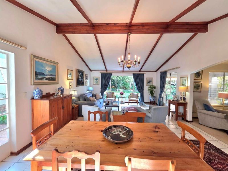 Spacious open-plan living and dining area featuring exposed timber ceiling beams, tiled flooring, and large glass doors providing natural light and garden access.