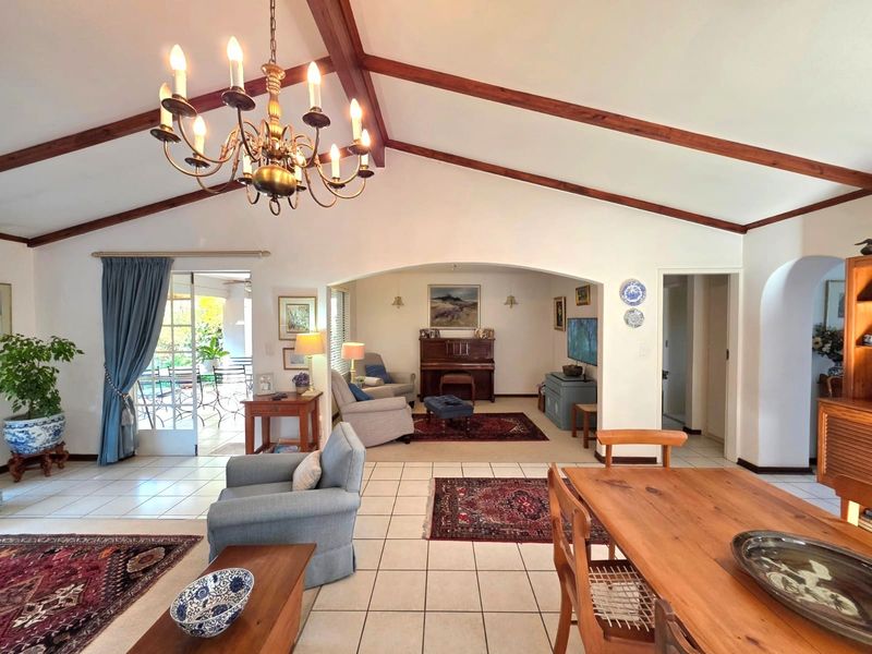Spacious open-plan living area featuring vaulted ceilings with exposed timber beams, ceramic tiled flooring, and an arched transition to an additional lounge space.