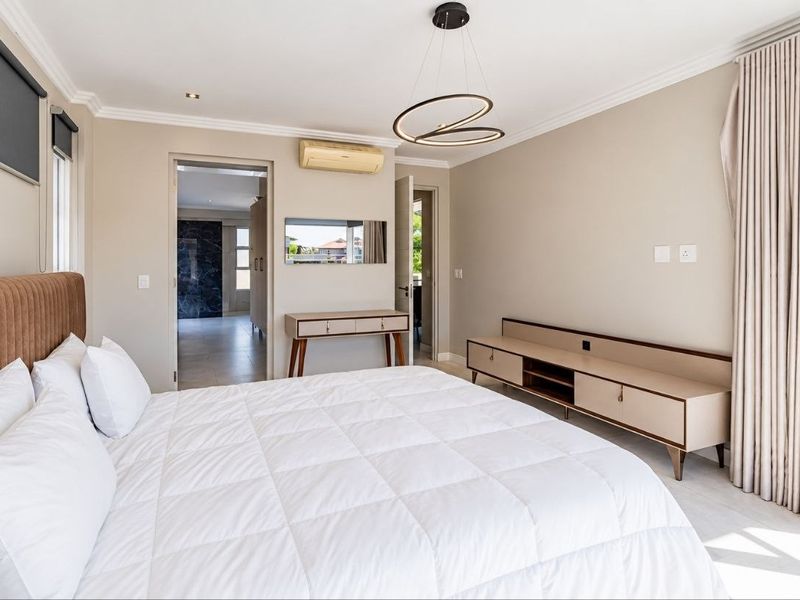 A well-maintained bedroom featuring neutral walls, crown molding, an integrated air conditioning unit, and large windows with roller blinds and floor-to-ceiling curtains.