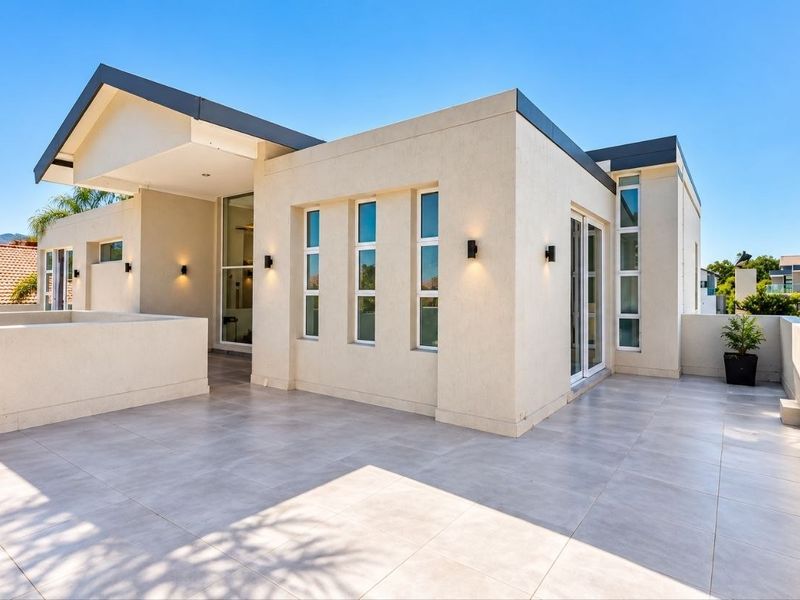 A spacious, modern balcony featuring clean tiled flooring, contemporary wall-mounted lighting, and large glass sliding doors providing seamless indoor-outdoor flow.