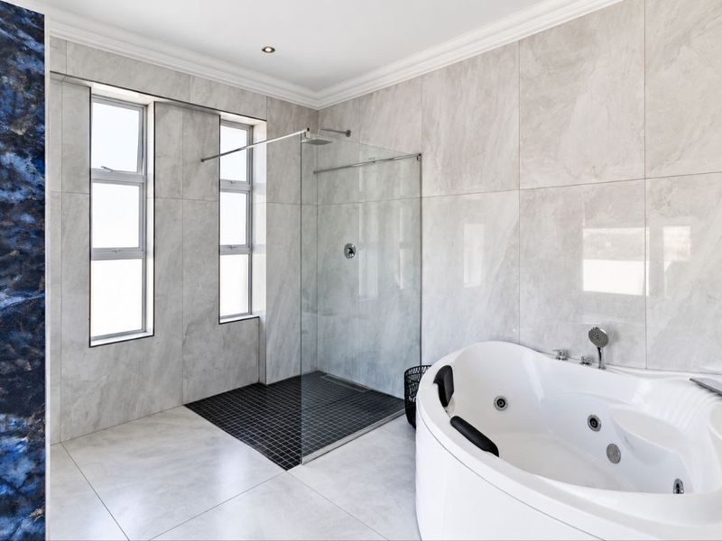 Modern bathroom featuring a spacious walk-in shower with glass screen, a corner jacuzzi bathtub, and elegant large-format wall tiling.