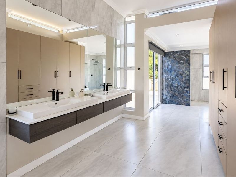 Modern, spacious bathroom featuring a double vanity, extensive built-in storage, large format tiling, and a striking blue feature wall with access to outdoor space.