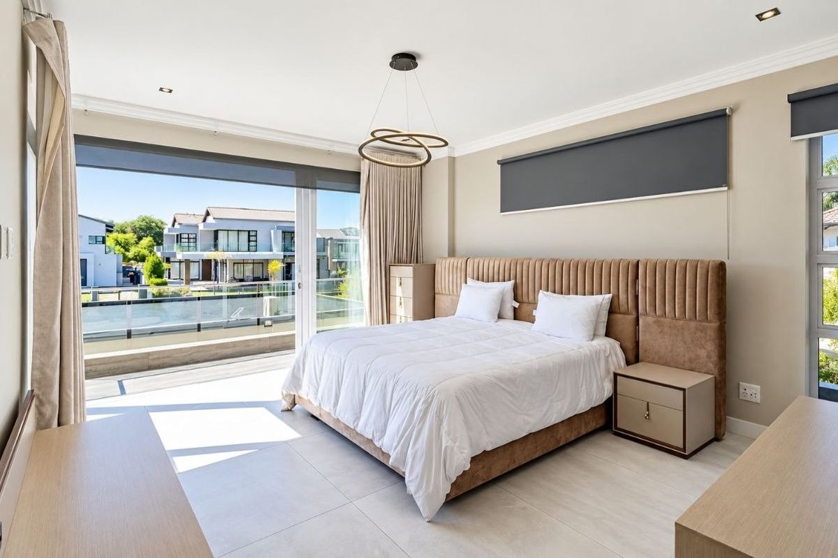 Spacious modern bedroom featuring large sliding glass doors leading to a balcony, neutral tiled flooring, and contemporary recessed lighting.