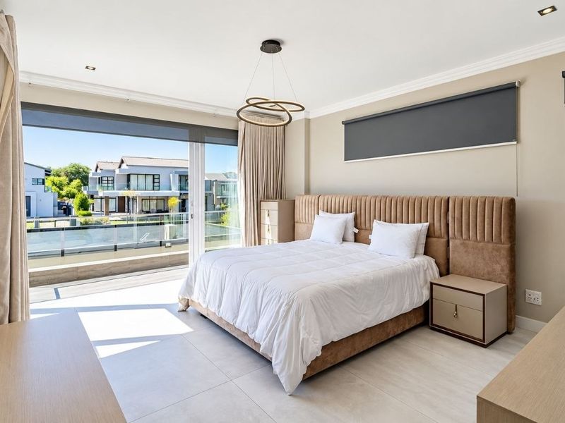 Spacious modern bedroom featuring large sliding glass doors leading to a balcony, neutral tiled flooring, and contemporary recessed lighting.