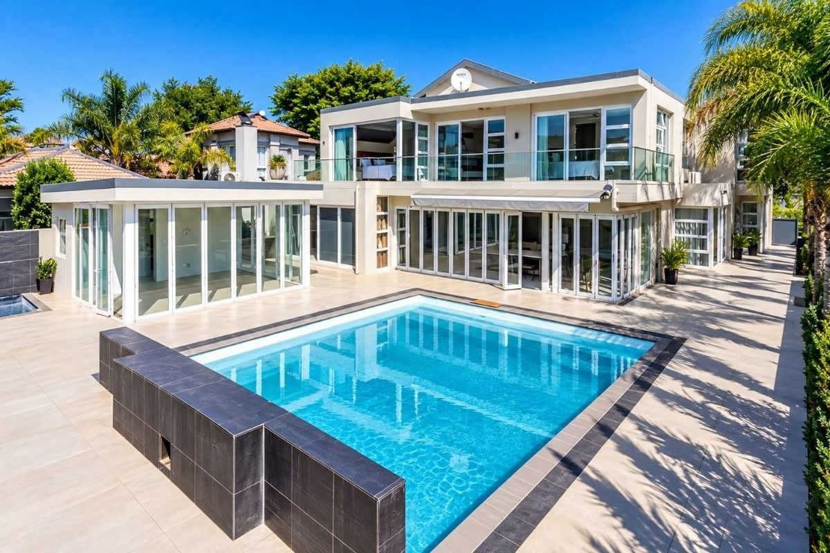 Rear view of a modern double-story house featuring a swimming pool, expansive tiled patio, and large glass sliding doors leading to the interior living spaces.