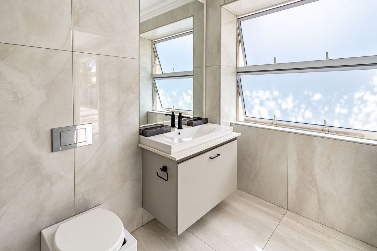 Modern bathroom featuring a wall-mounted vanity, ceramic basin, wall-mounted toilet, and large-format neutral wall tiles with ample natural light from awning windows.