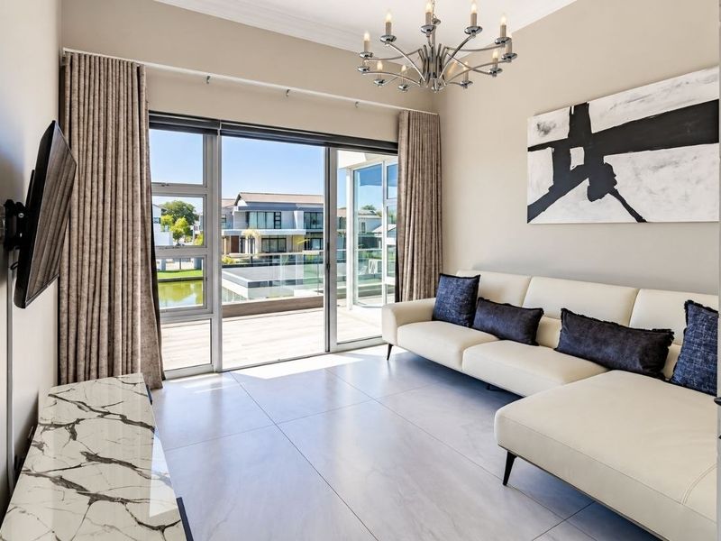 A bright and modern living room featuring large format floor tiles, a contemporary chandelier, and sliding glass doors opening to an outdoor deck area.