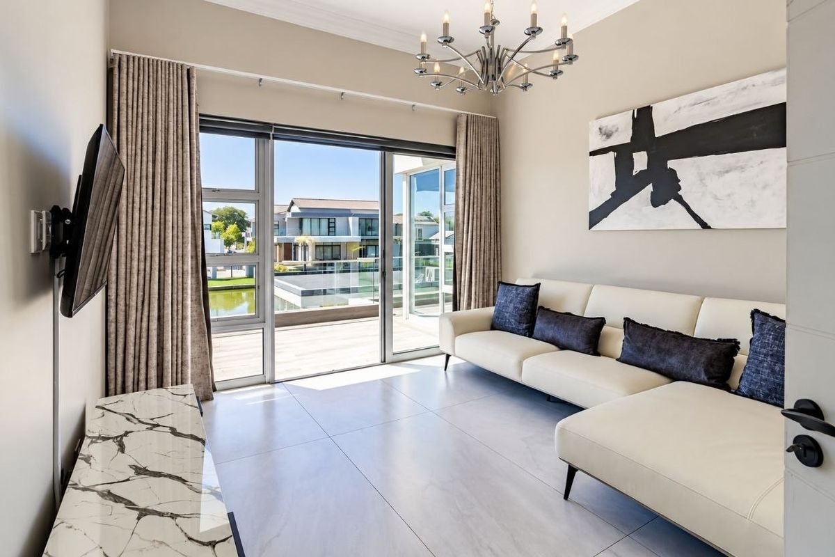 A bright and modern living room featuring large format floor tiles, a contemporary chandelier, and sliding glass doors opening to an outdoor deck area.