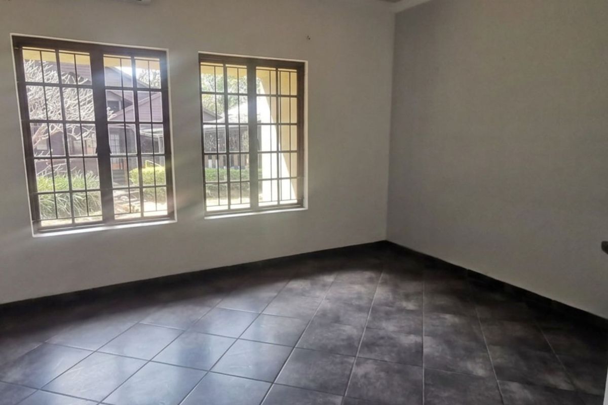 A vacant bedroom featuring dark tiled flooring, built-in cupboards, and windows fitted with security bars, offering a clean and neutral space.