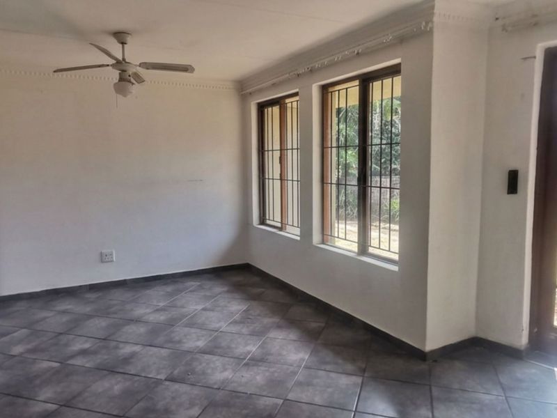 An empty living room featuring tiled floors, a ceiling fan, built-in storage, and direct access to the garden through a timber-framed glass door.