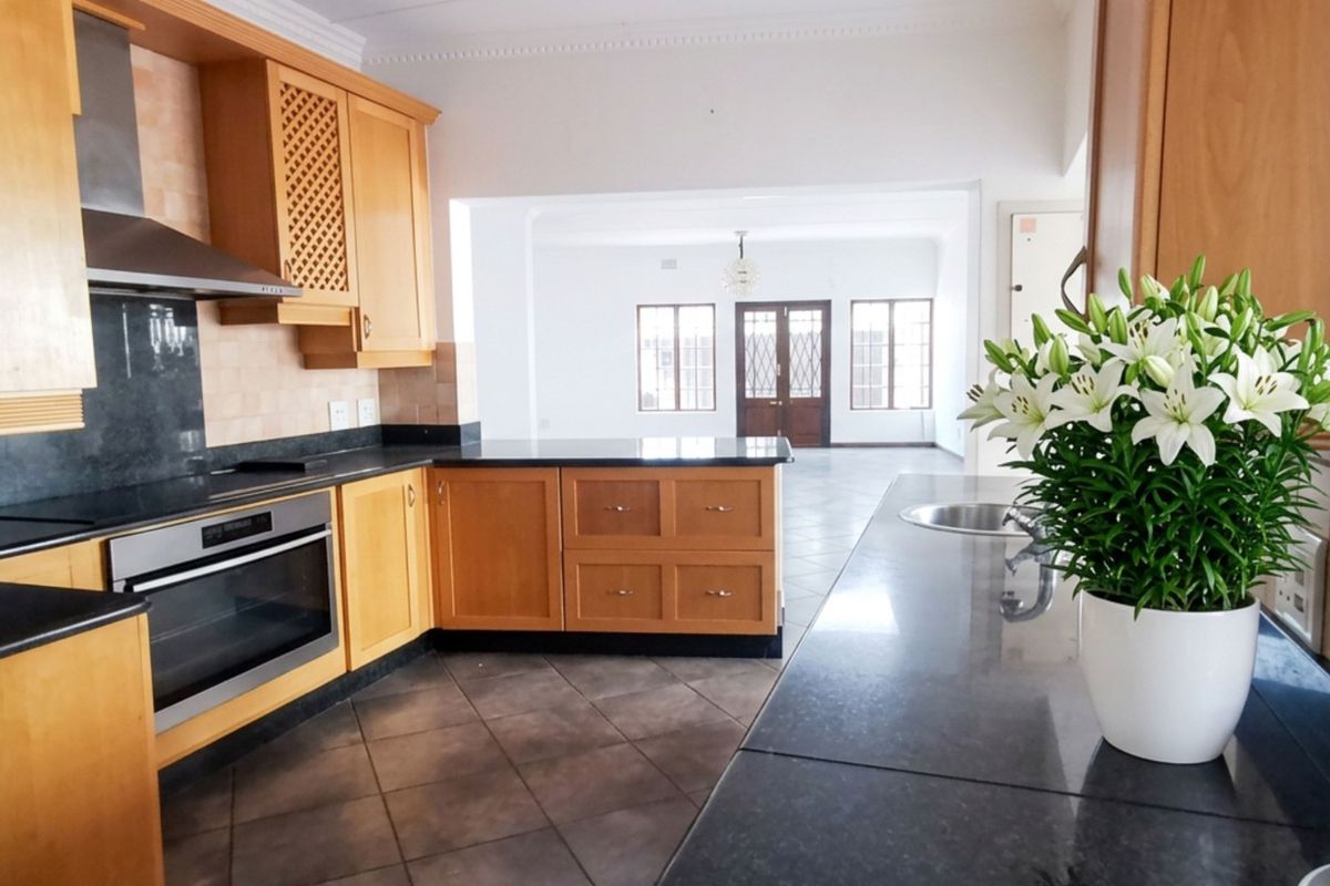 A functional kitchen featuring wooden cabinetry, granite countertops, built-in oven, and extractor fan, flowing into an open-plan living area.