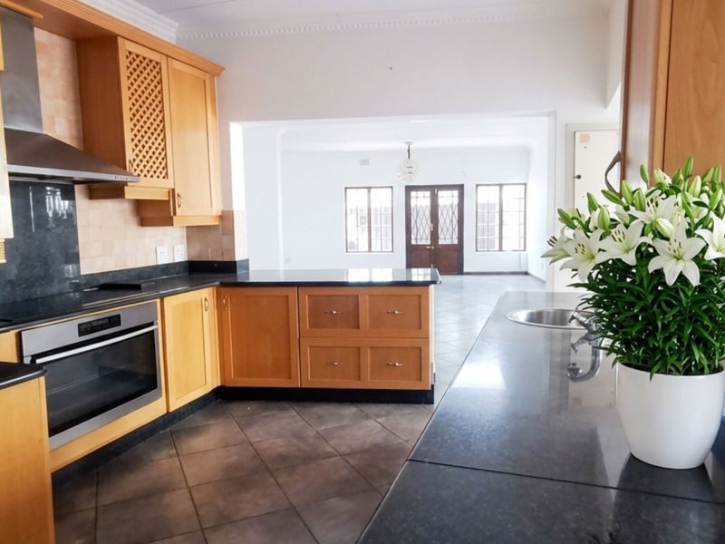 A functional kitchen featuring wooden cabinetry, granite countertops, built-in oven, and extractor fan, flowing into an open-plan living area.