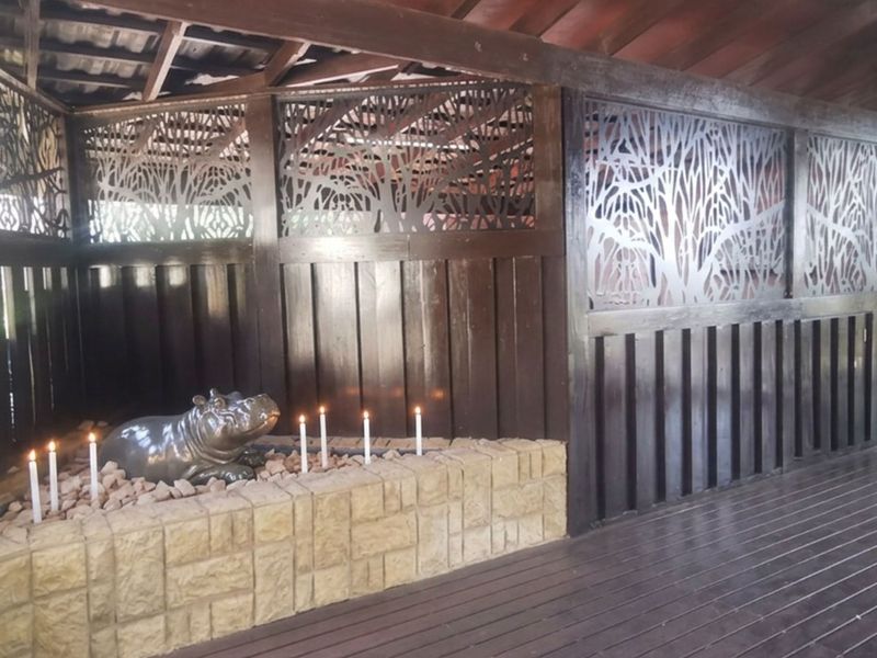 A covered outdoor patio featuring timber decking, decorative laser-cut privacy screens, and a stone-clad planter box under a timber roof structure.