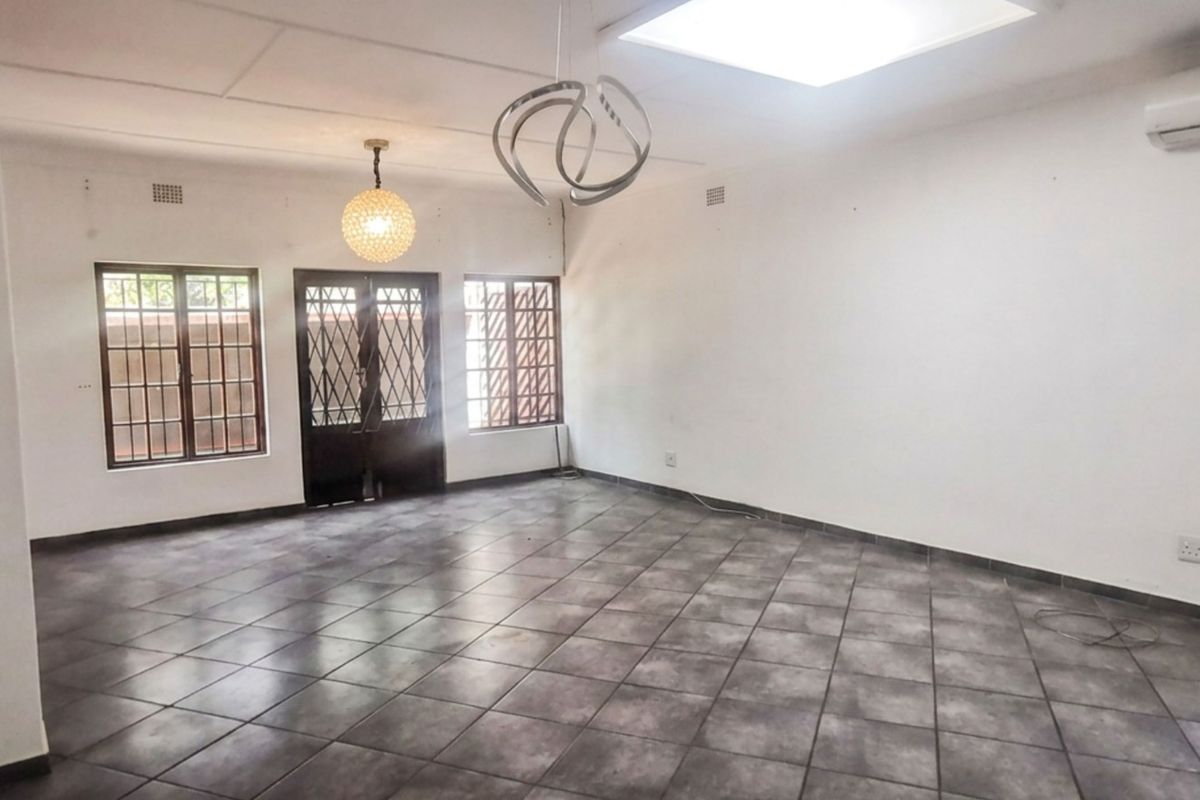 Spacious, empty living area featuring tiled flooring, security gates on windows and doors, and an installed air conditioning unit.